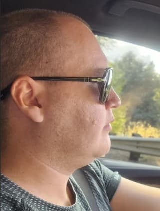 Side profile of a man with short hair wearing sunglasses while sitting in a car.